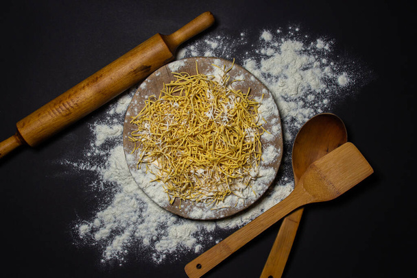 Egg noodles in flour on a black background. Dry homemade noodles on a wooden board. Traditional pasta - Foto, imagen