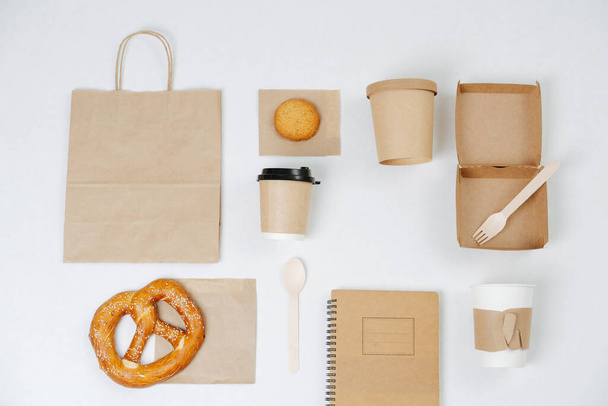 Paper eco friendly items arranged in composition. Carton compostable products over white. Cups, box, bag, cutlery, notepad completed with some pastry. - Fotoğraf, Görsel