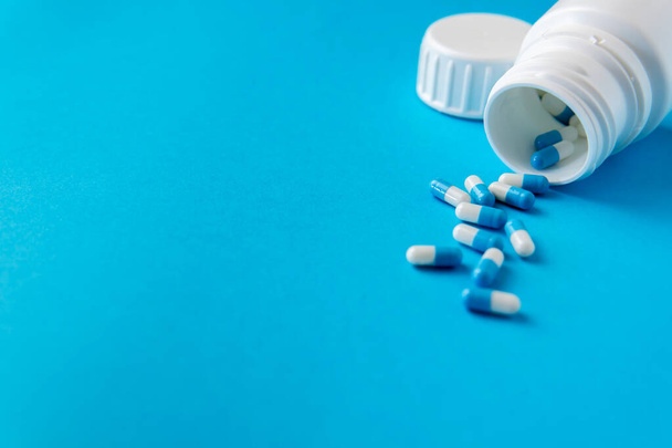 Léková lahvička s modrými a bílými tobolkami na modrém pozadí - Fotografie, Obrázek