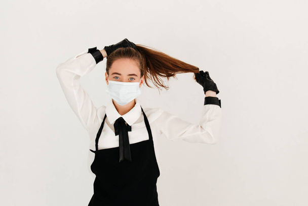 Mujer joven camarera en el trabajo, con mascarilla y guantes. Concepto medidas de seguridad - Foto, Imagen