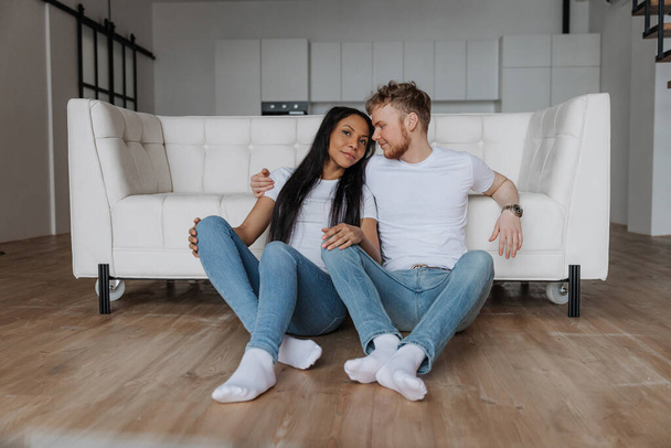 Jovem casal feliz sentado no chão em casa e olhando um para o outro  - Foto, Imagem