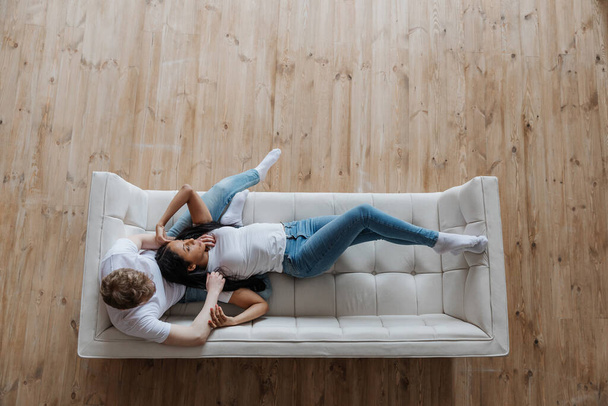 Blick von oben auf anhängliches junges multirassisches Paar beim Kuscheln auf dem Sofa - Foto, Bild
