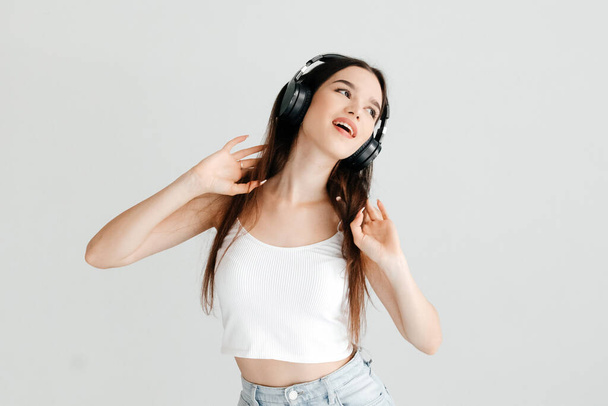 Emotive portrait of young woman wearing casual clothes - white top and jeans, black headphones, listening to pop music, having fun - Foto, afbeelding