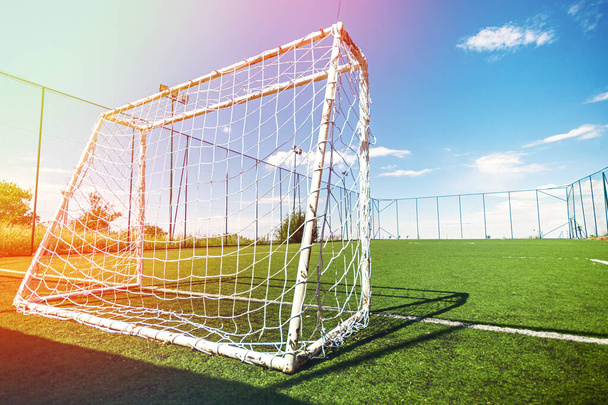 Ερασιτεχνικό γήπεδο ποδοσφαίρου με στόχο, πίσω όψη, φακό φωτοβολίδα και μπλε ουρανό. - Φωτογραφία, εικόνα