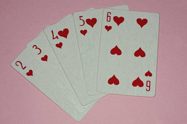 игральные карты с комбинацией стрит-флеш лежат на розовом столе - Фото, изображение