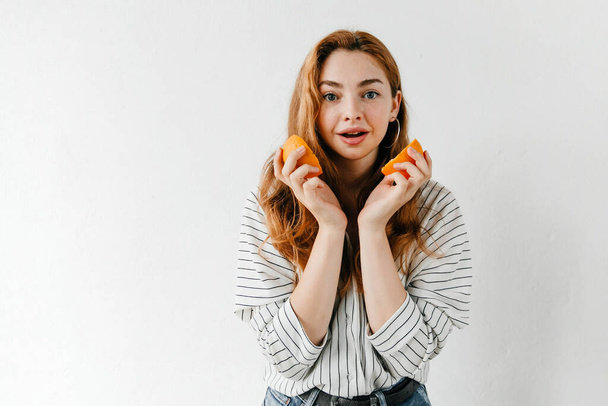 Usmívající se atraktivní dívka drží střih oranžová izolované na bílém - Fotografie, Obrázek