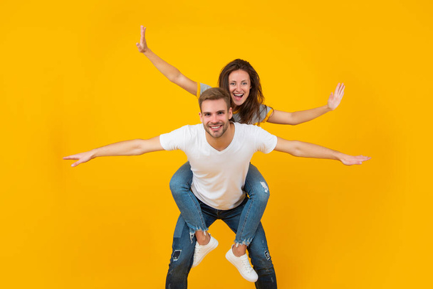 Happy couple in love of girl and man pretend flying doing piggyback ride yellow background, playful - Foto, afbeelding
