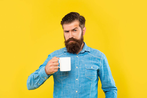Serious caucasian man holding mug yellow background, tea break - Photo, image