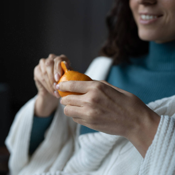 Smiling young woman peels juicy ripe tangerine, home eating seasonal fruits during winter months - Fotografie, Obrázek