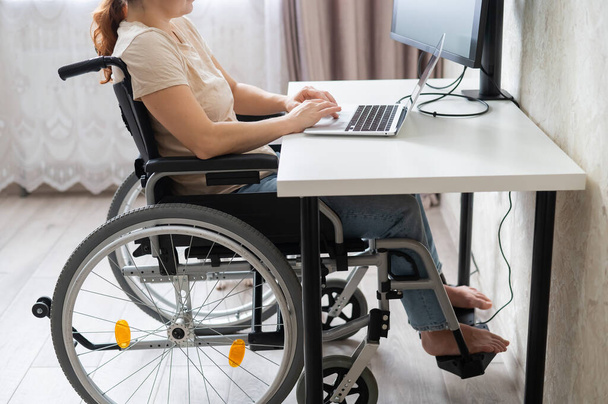 Blanke vrouw in een rolstoel aan het typen met een laptop van thuis. Werk op afstand voor mensen met een handicap. - Foto, afbeelding