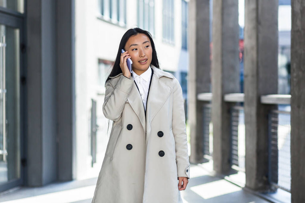 Beautiful and happy asian woman talking on the phone, chinese woman walking during a break near the office, business woman successful - Foto, Imagem