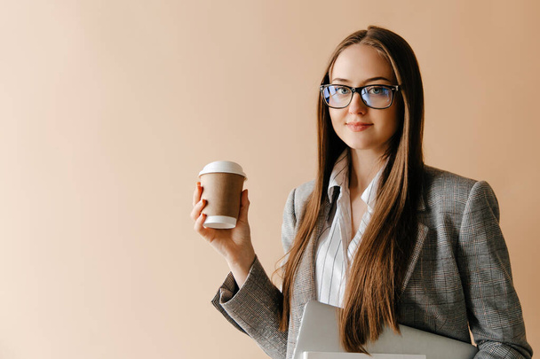 Улыбающаяся деловая женщина в очках, держащая ноутбук и забирающая чашку кофе. Концепция фриланса - Фото, изображение