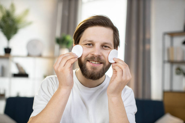 bearded guy smiling at camera and having fun while playing with cotton pads, covering his eye - Foto, Bild