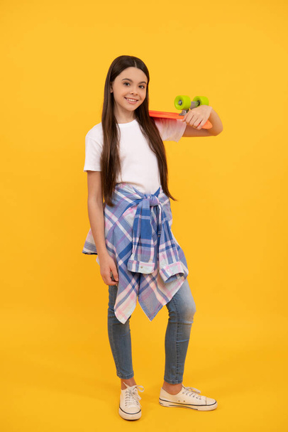 Happy teenage girl in teen casual holding pennyboard yellow background, skater girl - Fotoğraf, Görsel