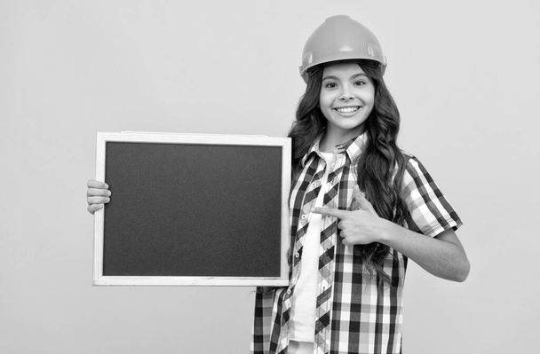 šťastný kluk v helmě ukazující prstem na školní tabuli s reklamou, kopírovací prostor, nabídka - Fotografie, Obrázek