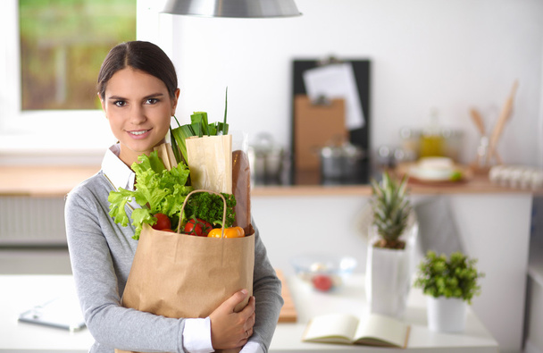 Young woman holding grocery shopping bag with vegetables Standing in the kitchen. - Foto, afbeelding