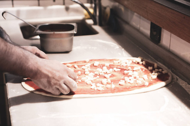 Pizza chef put sauce on base in a commercial kitchen - Foto, Bild
