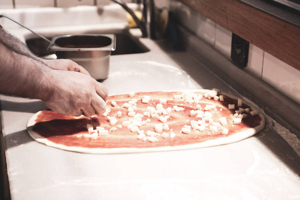 Pizza chef put sauce on base in a commercial kitchen - Φωτογραφία, εικόνα