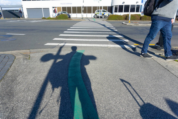Auckland Nowa Zelandia - Lipiec 12 2018; Cienie podróżnych, torby i nogi na lotnisku z pojazdem policyjnym przez przejście dla pieszych. - Zdjęcie, obraz