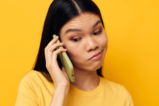Charming young Asian woman talking on the phone posing technology yellow background unaltered - Foto, Imagem