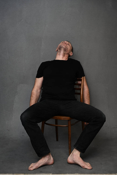 A full-length man sits on a chair with his head up. Vertical photo on a gray background - Zdjęcie, obraz