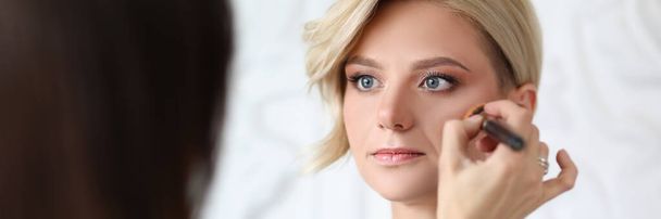Master make-up kunstenaar maakt make-up aan blonde vrouw - Foto, afbeelding