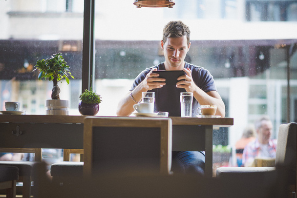 Молодий чоловік дивиться планшет у кафе
 - Фото, зображення