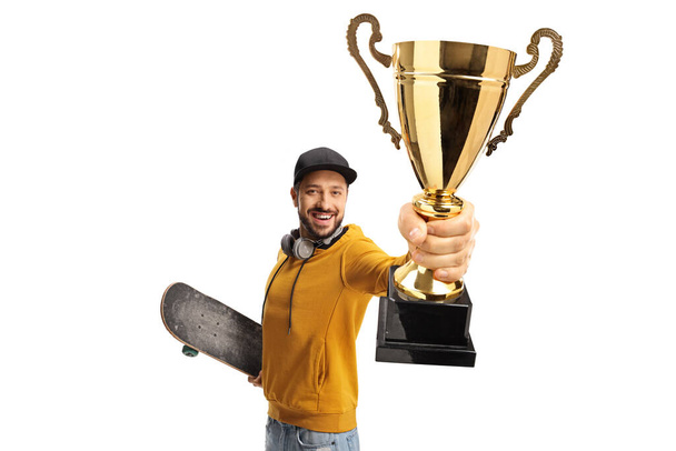 Happy guy with a skateboard holding a gold trophy cup isolated on white background - Foto, afbeelding
