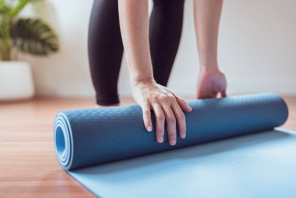 Woman roll out yoga mat for preparation, Female work out by exercise yoga in living room at home. - Photo, Image