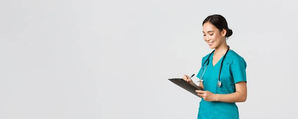 Healthcare workers, preventing virus, quarantine campaign concept. Beautiful smiling asian doctor, nurse running checkup in hospital, looking at clipboard with patient results, examine people - Photo, Image