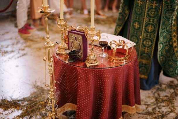 Крест, золотые короны, подсвечники и Библия на столе в церкви перед священником - Фото, изображение