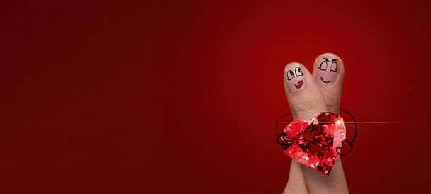 szczęśliwy palec para w miłości z malowane smiley i trzymać diamentowy pierścień kształt serca na czerwonym tle. - Zdjęcie, obraz