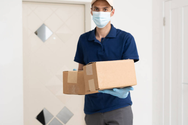 Delivery guy with protective mask and gloves holding box with groceries in front of a door - Фото, зображення