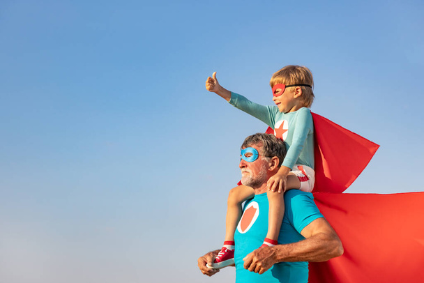 Superhero senior man and child playing outdoor. Super hero grandfather and boy having fun together against blue summer sky background. Family holiday concept. Happy Father's day - Foto, Imagen