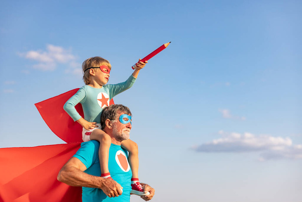 Superhero senior man and child playing outdoor. Super hero grandfather and boy having fun together against blue summer sky background. Family holiday concept. Happy Father's day - Fotoğraf, Görsel
