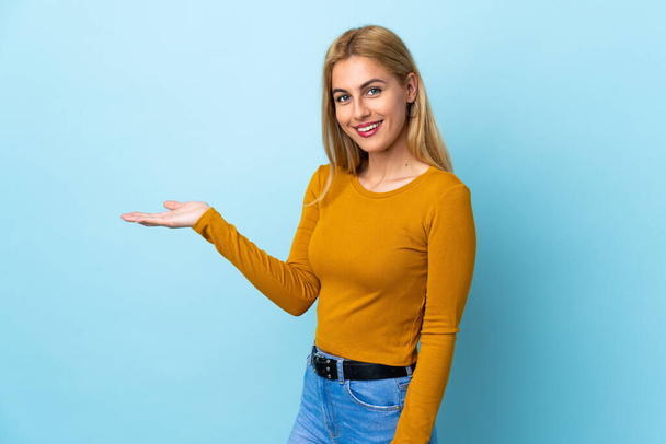 Young Uruguayan blonde woman over isolated blue background presenting an idea while looking smiling towards - Фото, зображення