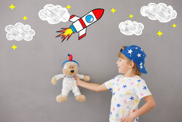 Happy child playing with teddy bear at home. Kid pretend to be astronaut. Imagination and children dream concept - Photo, Image