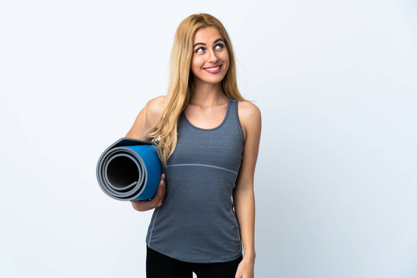 Young sport woman going to yoga classes while holding a mat over isolated white background looking up while smiling - Valokuva, kuva