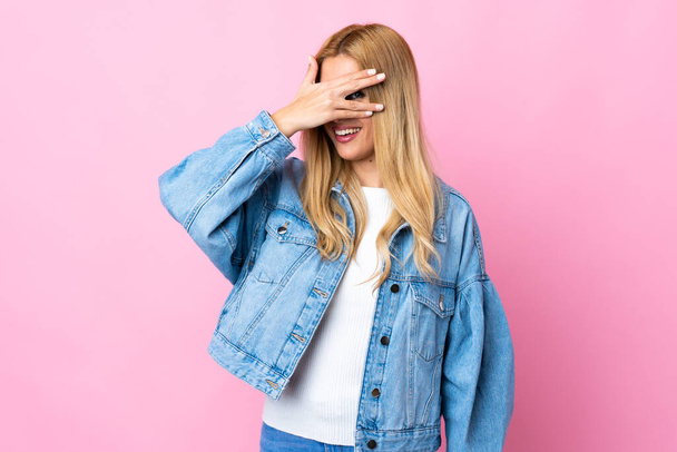 Young Uruguayan blonde woman over isolated pink background covering eyes by hands and smiling - Photo, image