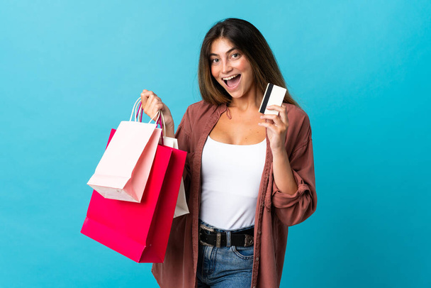 Young caucasian woman isolated on blue background holding shopping bags and a credit card - Фото, изображение