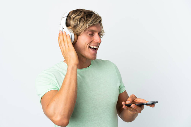 Hombre inglés sobre fondo blanco aislado escuchando música con un móvil y cantando - Foto, imagen