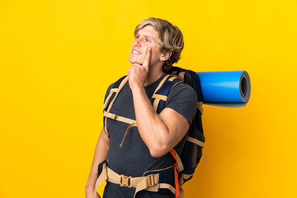 Young mountaineer man over isolated yellow background thinking an idea while looking up - 写真・画像