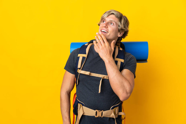Jovem montanhista homem sobre isolado fundo amarelo olhando para cima enquanto sorri - Foto, Imagem