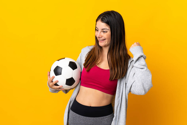 Junge kaukasische Frau auf gelbem Hintergrund mit Fußballball, der einen Sieg feiert - Foto, Bild