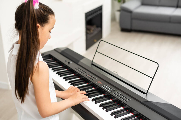 Красива маленька дівчинка грає на піаніно в світлій кімнаті
 - Фото, зображення