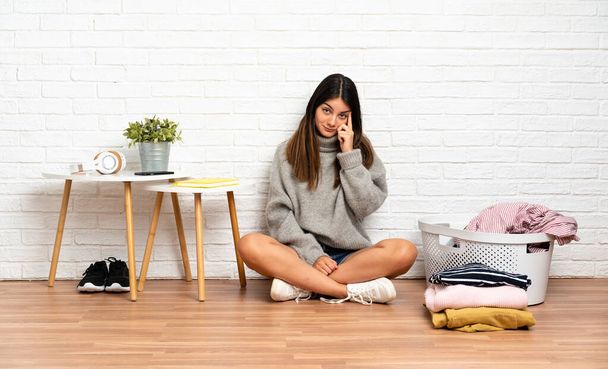 Mladá žena sedí doma na podlaze s košem na šaty a přemýšlí o nápadu - Fotografie, Obrázek