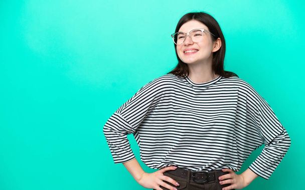 Young Russian woman isolated on green background posing with arms at hip and smiling - Фото, изображение