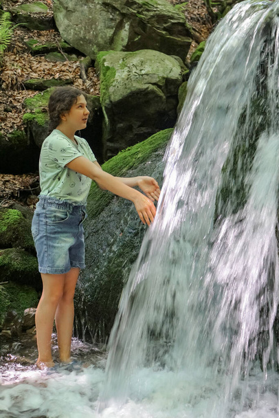 teenage girl near a waterfall on a mountain stream in the Carpathians in summer - Photo, image