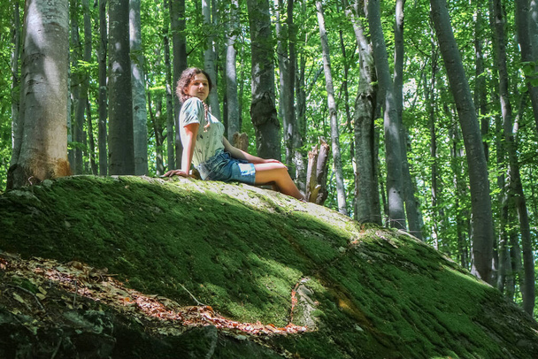 dospívající dívka sedí v létě na velkém mechovém kameni v lese, v Karpat - Fotografie, Obrázek