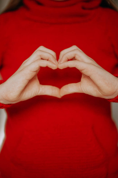 a person in a red sweater shows a heart sign with his hands. valentine's day holiday symbol - Foto, Imagem